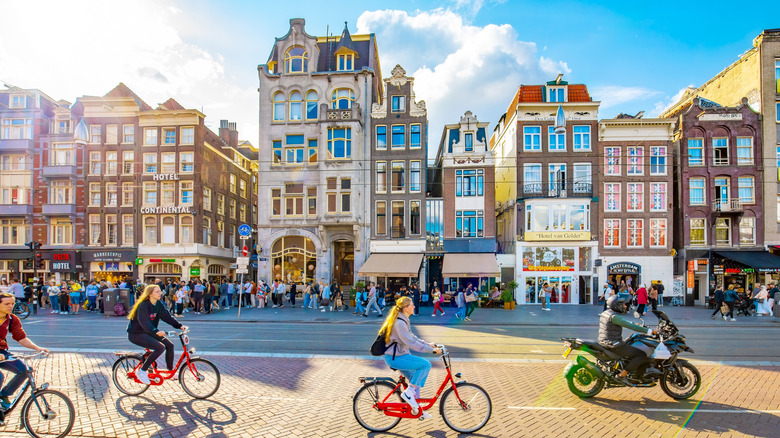 Cyclists, pedestrians, and motorists on scooters moving through the streets of Amsterdam against the city's iconic architecture