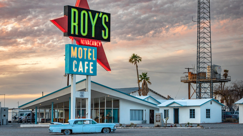 The Roy's Motel and Cafe building and neon sign in Amboy, California with an antique car parked out front at sunset