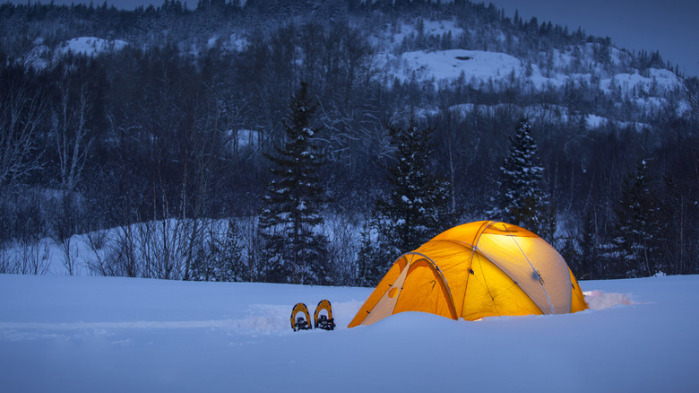 A tent in the snow at dusk lit up with lights inside.