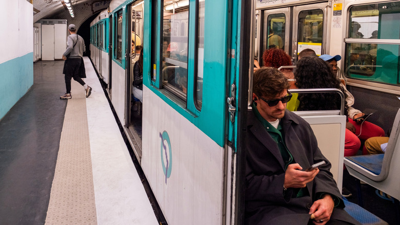 Commuter wearing glasses on his phone sitting on a pull-down seat in a Parisian Metro car