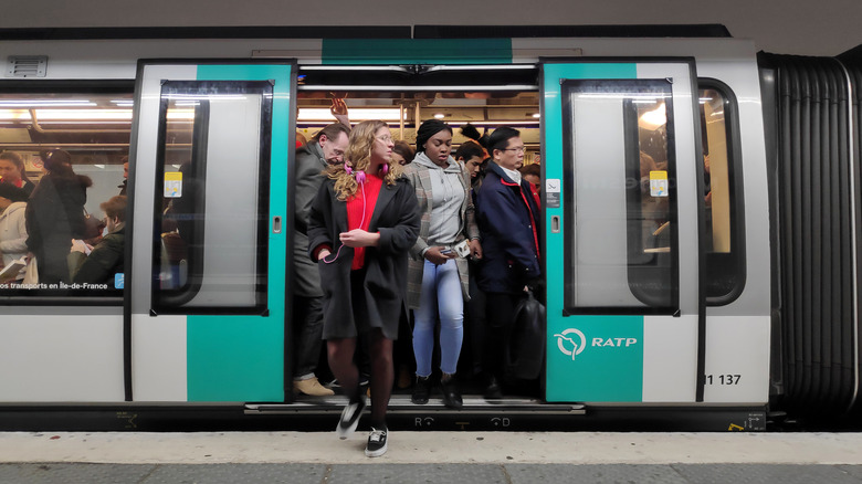 Woman in a coat and red shirt exiting a full Metro carriage in Paris
