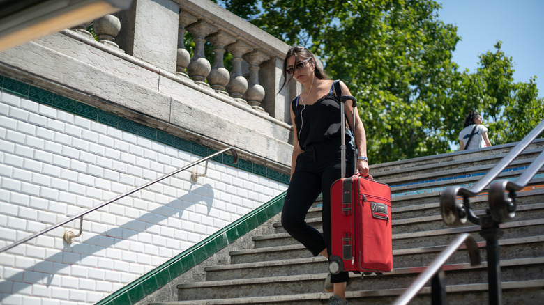 Woman carrying a red luggage down the stairs of the Metro in Paris