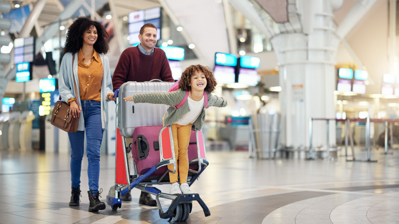 A couple with their young child moving through an airport with luggage on a trolley