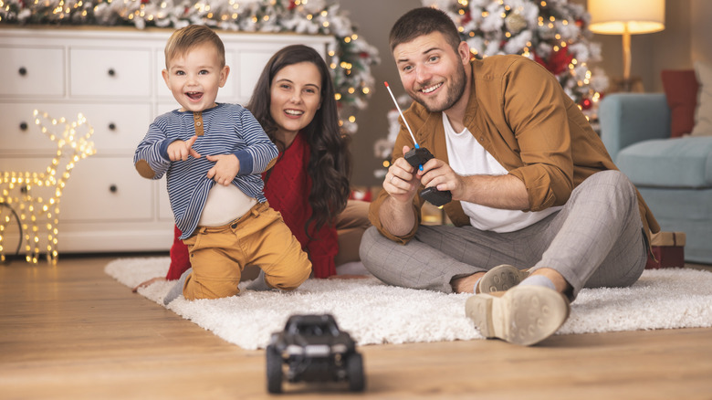 A family with a young child plays together with a remote-controlled car in a living room