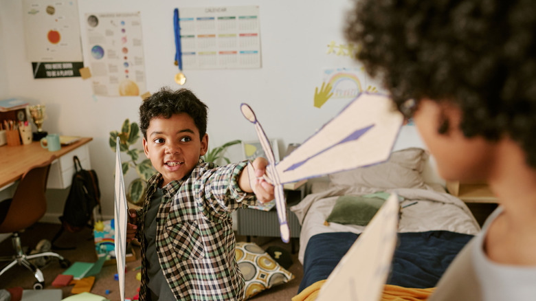 Two children play with cardboard swords and shields inside a bedroom