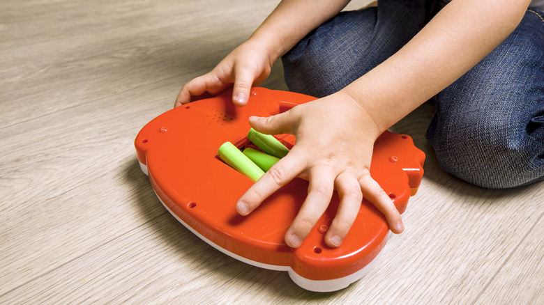 A child taking batteries out of the back of a plastic toy
