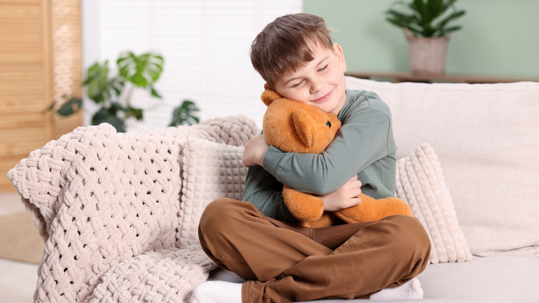 A young boy hugs a Teddy bear while sitting on a sofa