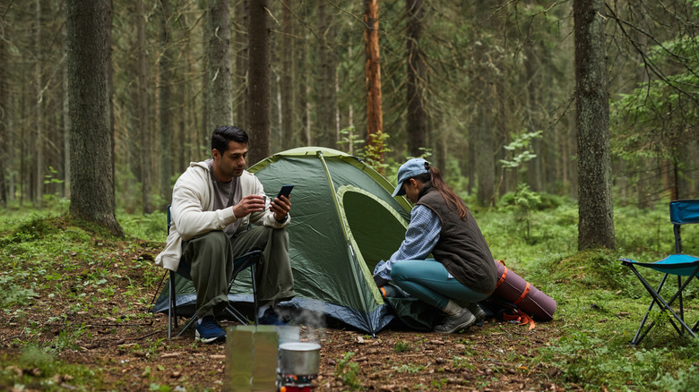A couple at a forested campsite with a green tent