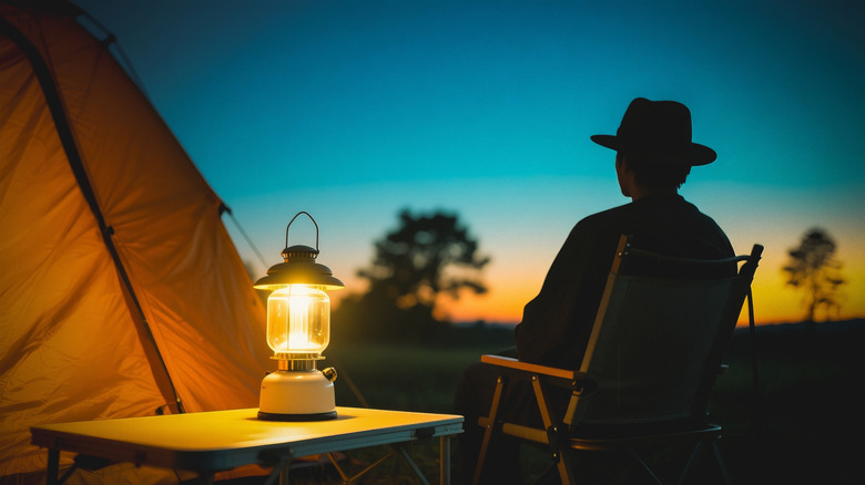 Silhouette of person sitting outside with a camping lantern next to them