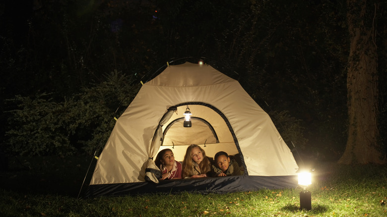 Kids in a tent with a camping lamp outside