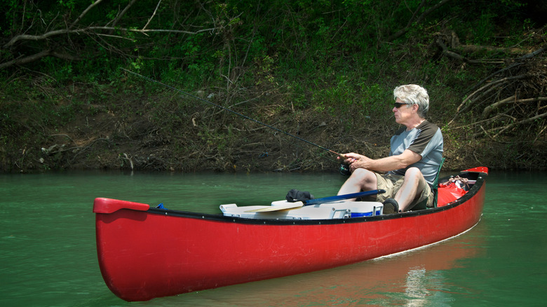 Man with gray hair in a red canoe holding a fishing pole