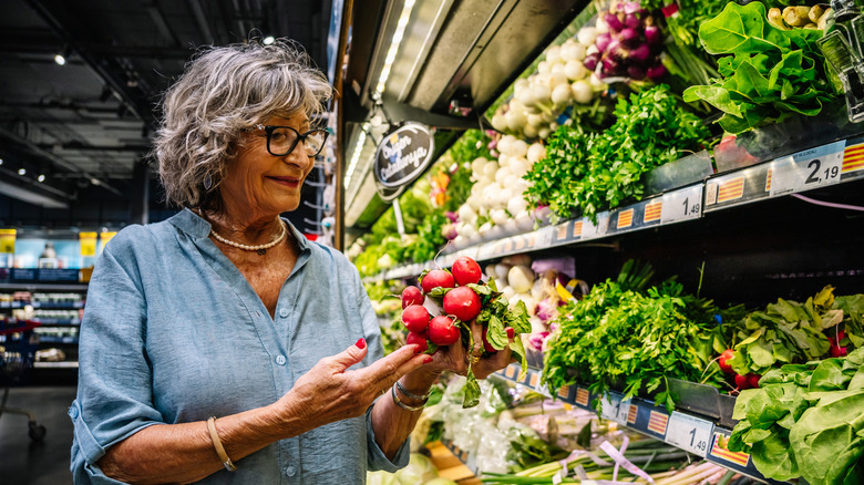 Woman with gray hair holding vegetables in grocery store produce section