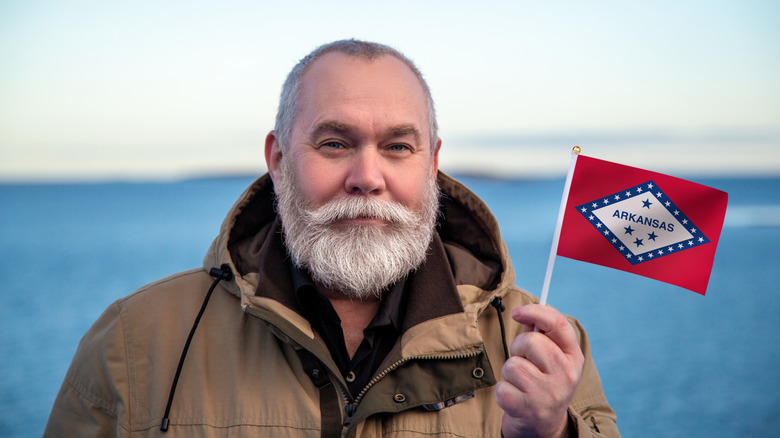Older man with gray hair holding a small Arkansas state flag