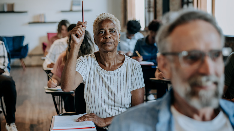 People in class and woman at desk raising her hand