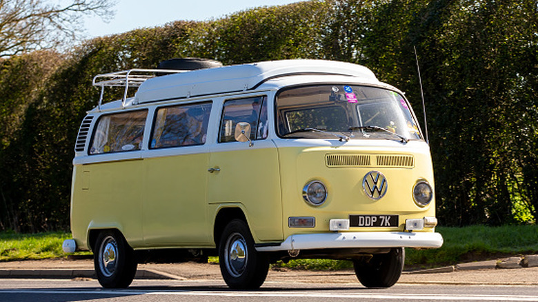 A yellow and white 1972 VW Camper Van driving down the road.