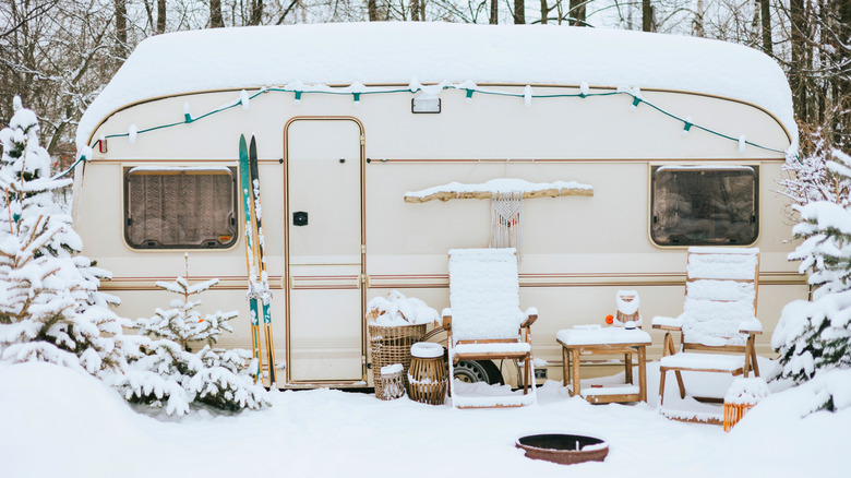 RV with chairs and skis covered in snow in the forest