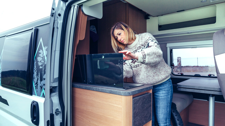 Woman cleans an appliance in an RV with the door open.
