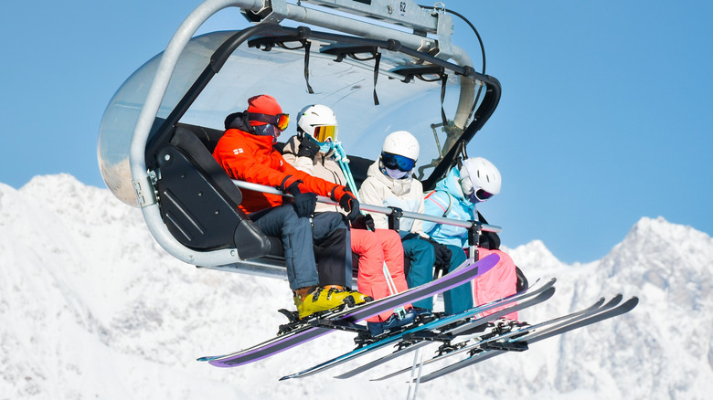 four skiers sharing a chair lift against a background of snowy mountains and blue sky