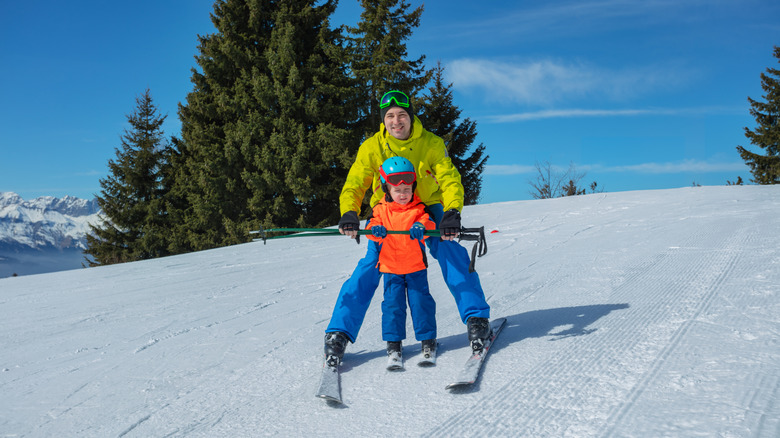 An adult teaching a toddler to ski on a gentle slope
