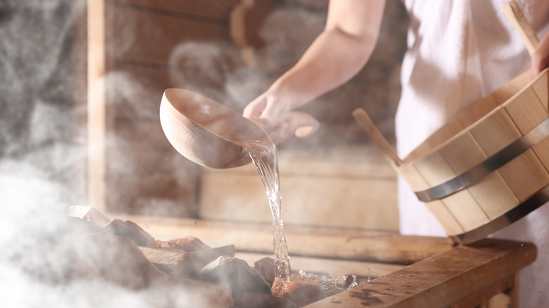 Woman pouring water onto stones to make steam in a sauna