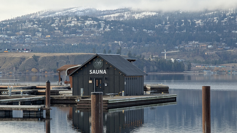 Exterior of Löyly as it floats in the water with city and forest behind it