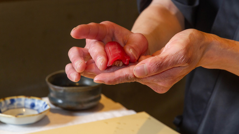 A sushi chef's hands carefully shaping a small piece of nigiri