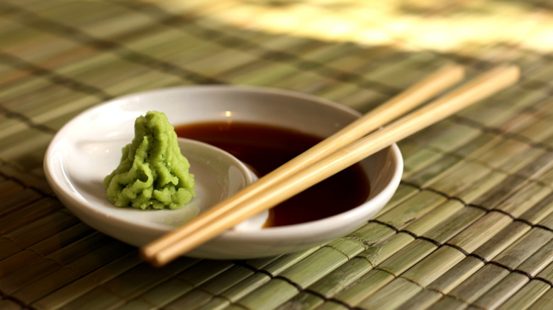 A dish of soy sauce and wasabi with chopsticks for sushi dipping on a rolled out bamboo food mat