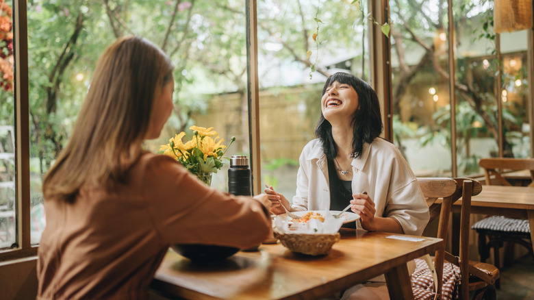 Two women laughing and eating at a restaurant in Thailand.