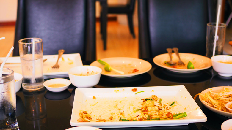 A table covered in dirty dishes and leftover Thai food on the serving plate.