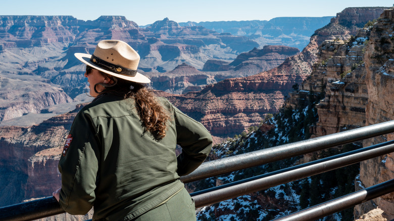 Park ranger leaning against a railing looking at the Grand Canyon