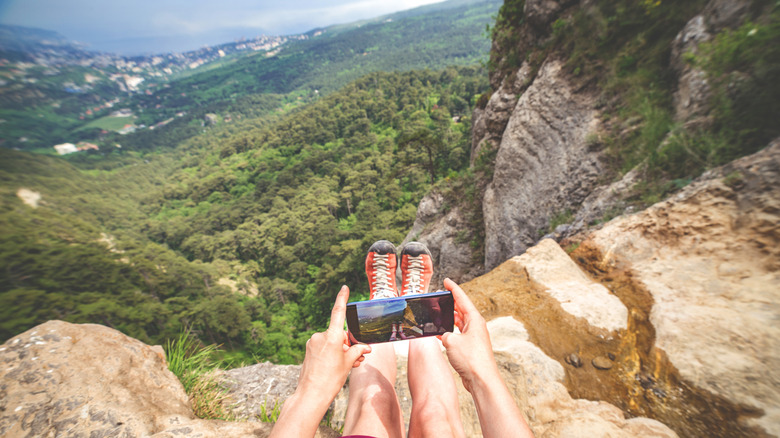 Person sitting on the edge of a cliff taking a photo