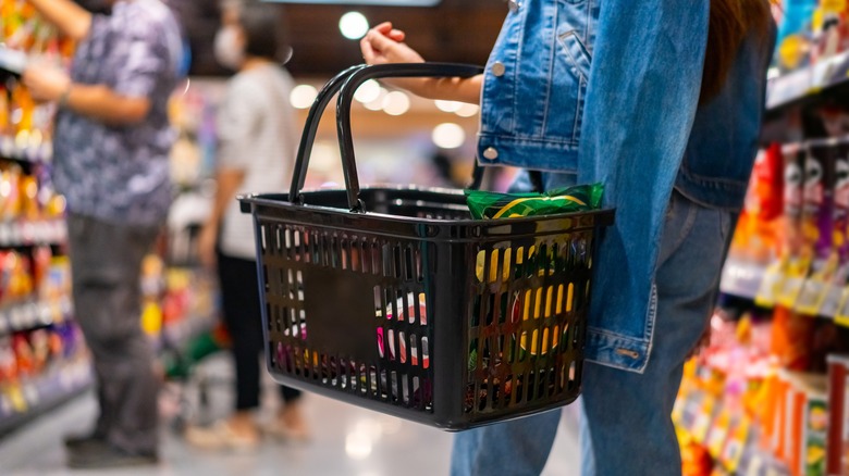 A medium shot of a person holding a shopping basket while standing in a grocery store aisle