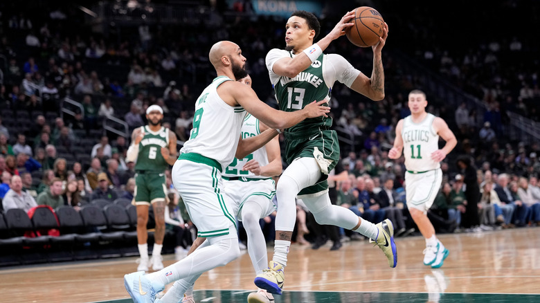 A Milwaukee Bucks player drives the ball against a Boston Celtics player with a crowd of spectators in the background.