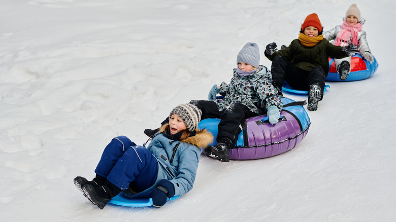 Four children snow tubing down a snowy mountain slope.