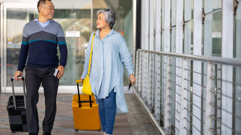 Older couple walking with wheeled luggage