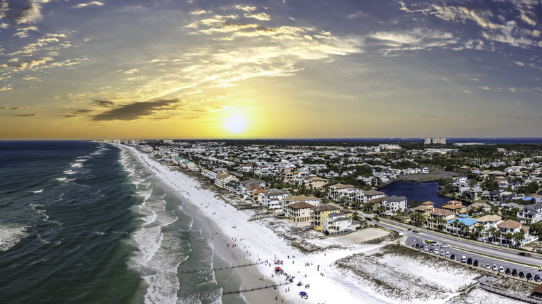 A sunny coastal scene with homes along the beach and people enjoying the ocean waves.