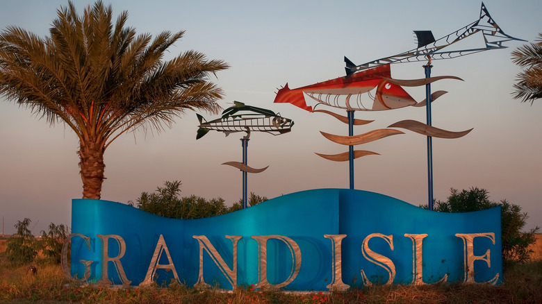 Grand Isle town sign with a palm tree and metal fish sculptures.