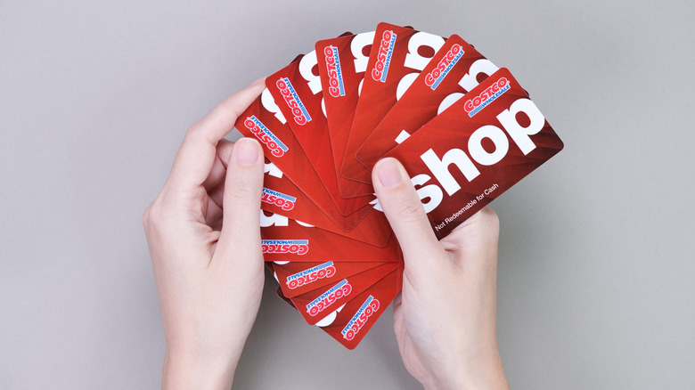 Hands holding several red-and-white Costco shop cards