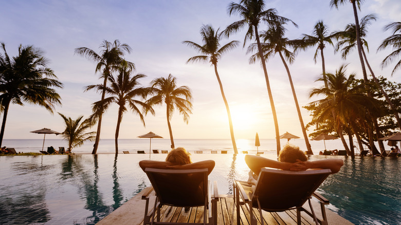 Couple lounging by a pool at a luxury beachfront resort, enjoying the sunset