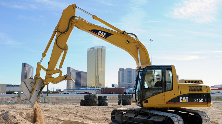 A tourist digs a hole with a yellow excavator in front of the Las Vegas skyline.