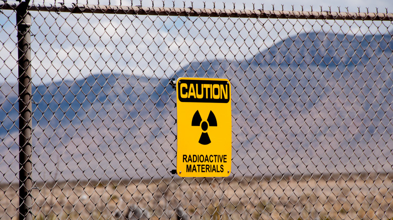 A wire fence with a yellow sign reading "CAUTION RADIOACTIVE MATERIALS" in front of arid mountains.