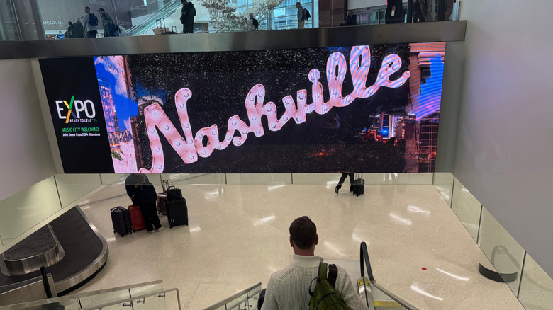 A person descends on an escalator in front of a "Nashville" LED banner inside Nashville airport