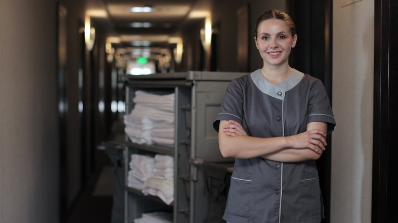 A smiling woman working in housekeeping standing in a hotel corridor next to towels.