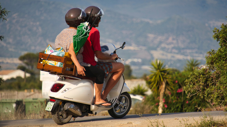 A couple wearing helmets on a Vespa in Porto Pino, Italy