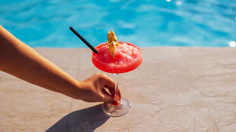 Hand holding a cocktail glass by the pool