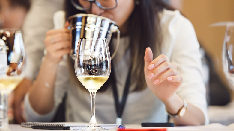 Someone using a spittoon during a wine tasting with a glass of white wine in the foreground
