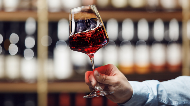 A sommelier holds out glass of red wine correctly, by the stem, swirling the contents