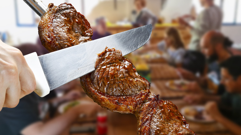 A Gaucho at a Brazilian steakhouse slicing picanha off a skewer in the dining room