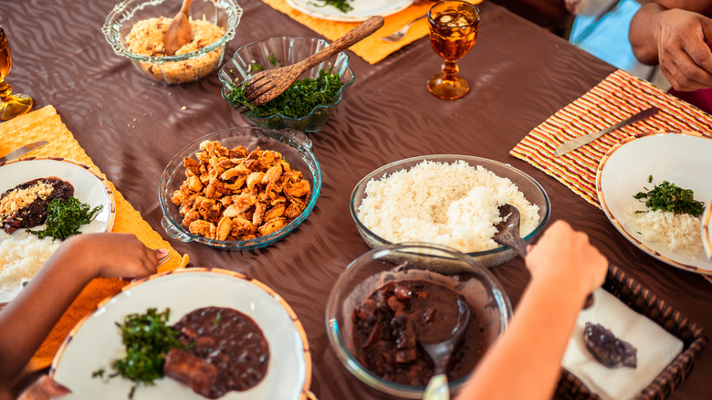 A home dinner table in Brazil, with hands serving up feijoada