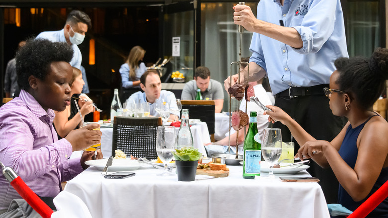 A dinner table at a Brazilian churrascaria with a gaucho carving meat tableside